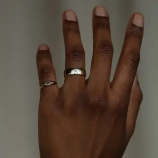 Close‑up of thick, rounded yellow gold ring with a clean row design and a small princess‑cut diamond inset flush with the surface.