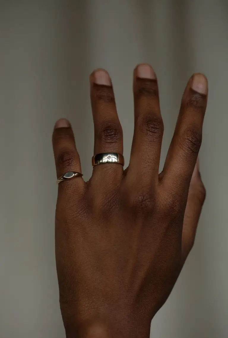 Close‑up of thick, rounded yellow gold ring with a clean row design and a small princess‑cut diamond inset flush with the surface.