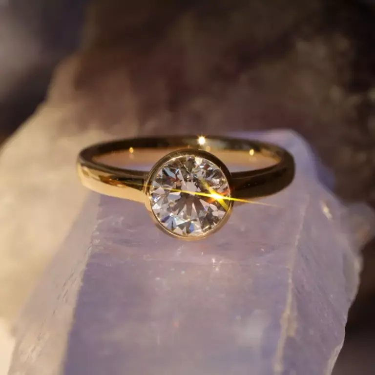 Close-up of the Tessa Bezel Round Solitaire Engagement Ring, highlighting the clean lines of the 14K yellow gold band and the brilliance of the 1.5ct diamond.