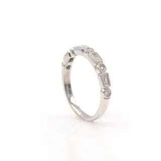 A slim white gold band with .17 ct total weight of sparkling round brilliant diamonds arranged midway around the ring. Each stone is meticulously bezel-set and bordered by fine milgrain detailing, enhancing the band’s refined, vintage aesthetic.