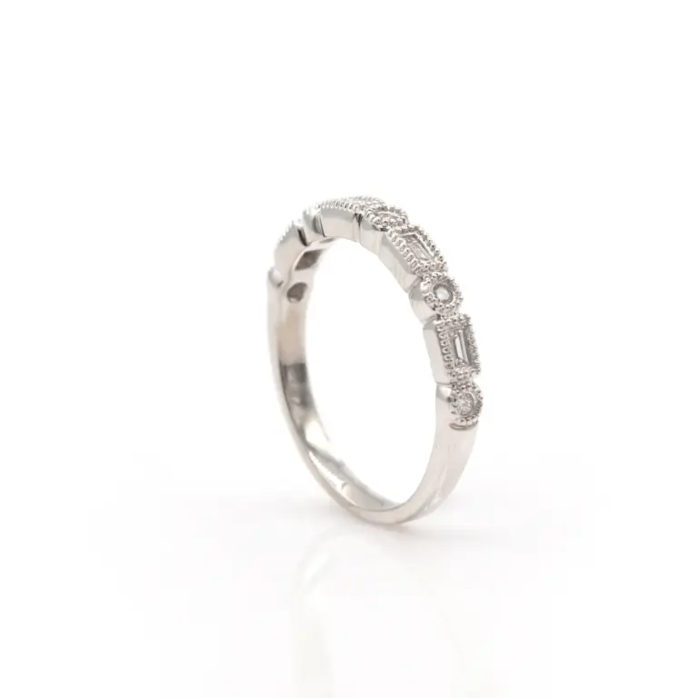 A slim white gold band with .17 ct total weight of sparkling round brilliant diamonds arranged midway around the ring. Each stone is meticulously bezel-set and bordered by fine milgrain detailing, enhancing the band’s refined, vintage aesthetic.