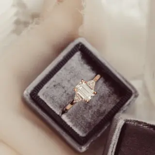 Refined three‑stone ring in 10K, 14K, or 18K yellow/white/rose gold showcasing an emerald‑cut moissanite center and trillion‑cut side stones