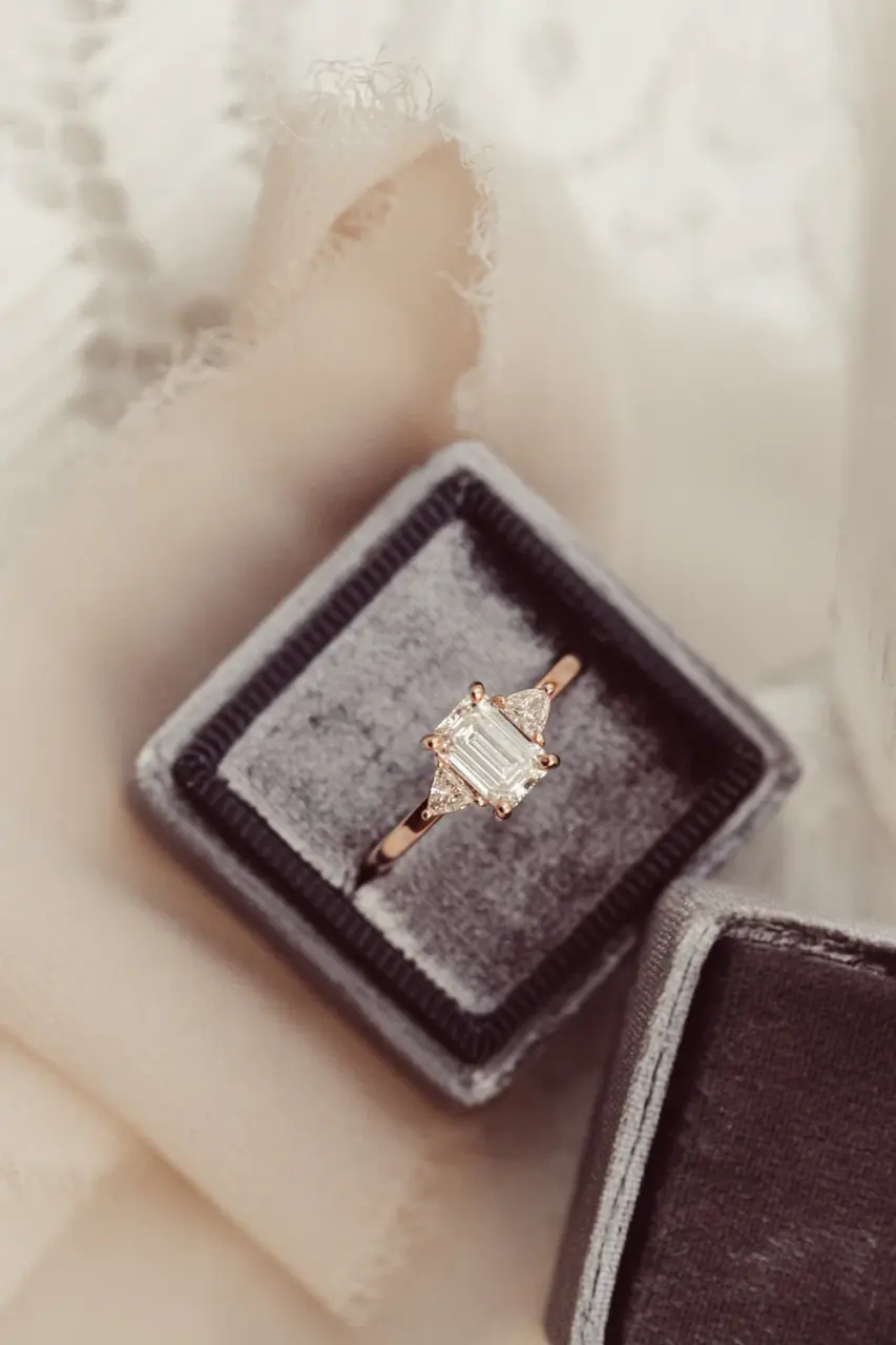 Refined three‑stone ring in 10K, 14K, or 18K yellow/white/rose gold showcasing an emerald‑cut moissanite center and trillion‑cut side stones
