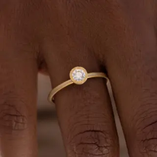 Close-up of Audry Rose's 18k Brushed Bezel Diamond Solitaire Ring showcasing the unique golden brushstroke bezel setting