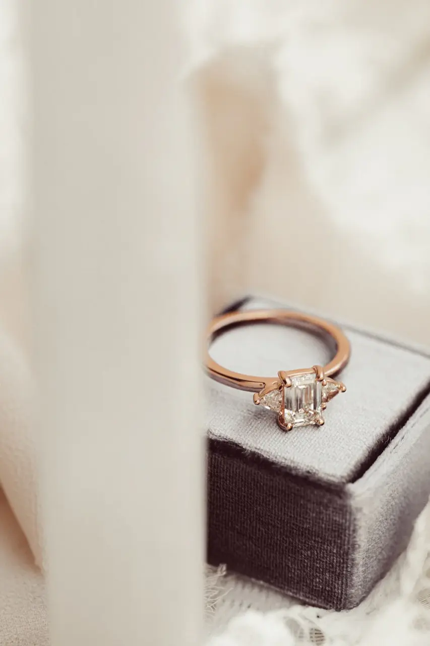 Close-up of emerald‑cut 1.0 ct colorless (DEF), VVS clarity moissanite with trillion‑cut side stones in a gold three‑stone engagement ring