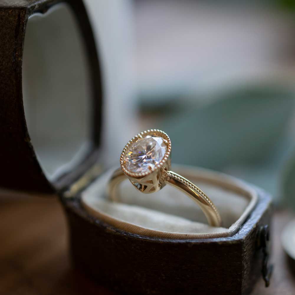 Marilyn Brogan 1.5 ct oval Art Deco diamond ring displayed on stand in 14k gold, highlighting the refined milgrain detailing, geometric cage settings, and sapphire accent stones.