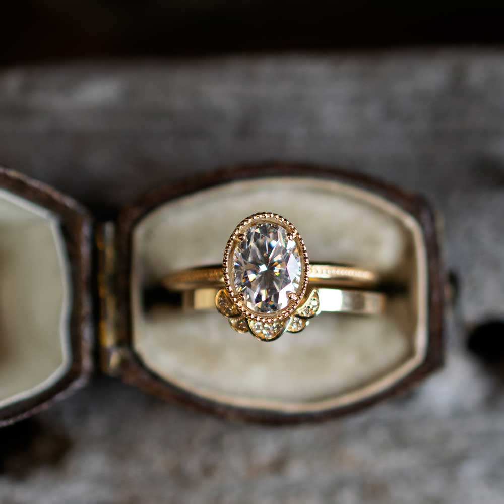 Hand wearing Marilyn Brogan’s 1.5 ct oval Art Deco diamond ring in yellow gold, showcasing elegant milgrain band and vintage-inspired geometric setting.