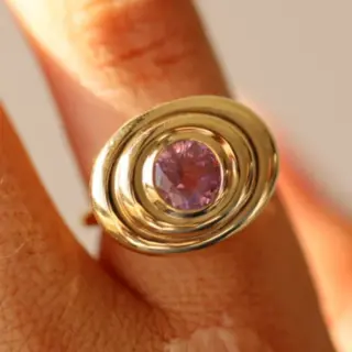 The 1.50ct Pink Sapphire In-Orbit Ring on a finger, featuring a 0.91ct oval pink sapphire in a contemporary 14k yellow gold setting.