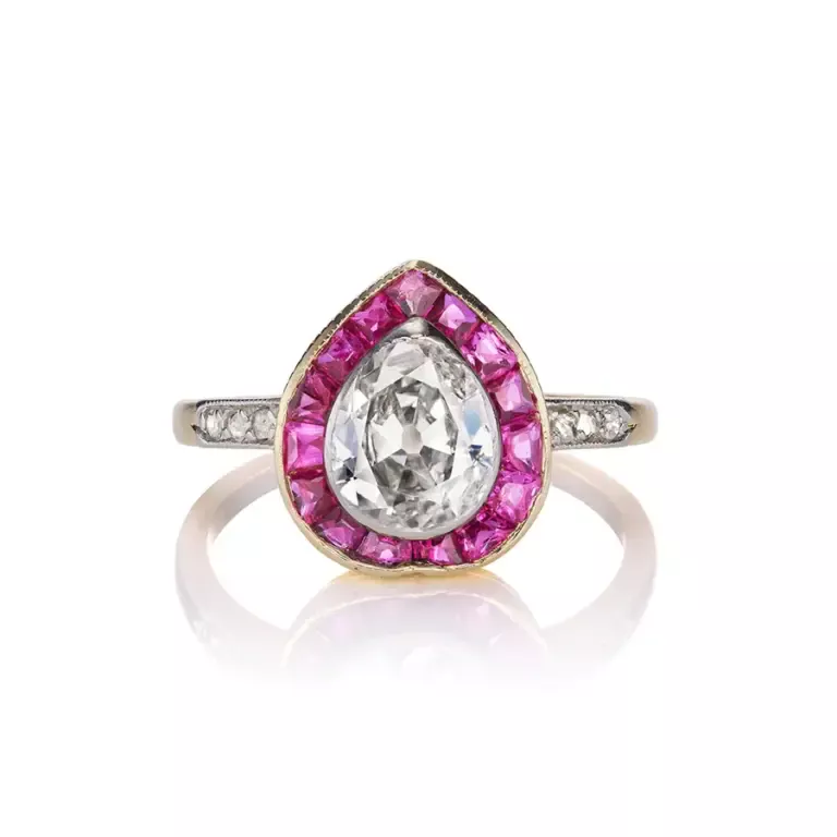 Vintage Edwardian-era engagement ring featuring a 0.80ct pear-cut diamond surrounded by a ruby baguette halo and diamond-accented shoulders in platinum and 18kt yellow gold setting.