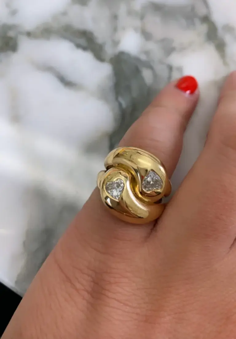 Close-up of Brent Neale's Knot Ring showcasing two heart-shaped diamonds set in a polished 18K yellow gold knot design.