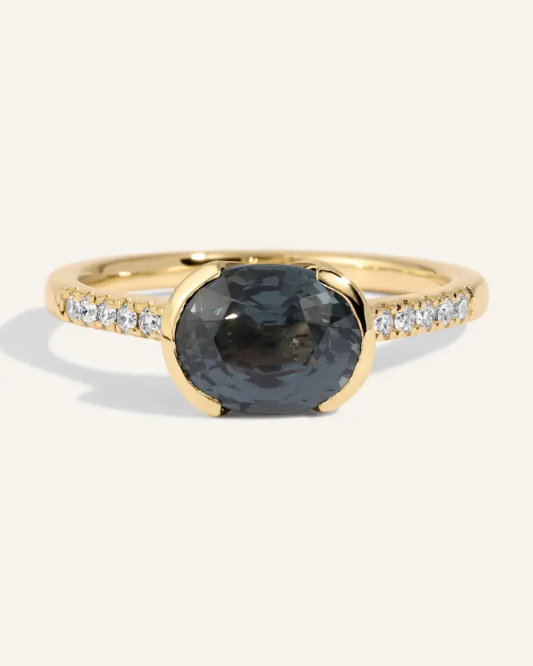 Detailed view of the Estrada Ring: a 2.31 ct dark gray‑blue spinel mounted side‑to‑side in a half‑bezel 14k gold setting, enhanced by a row of .09 ctw SI G‑H diamonds covering half the band