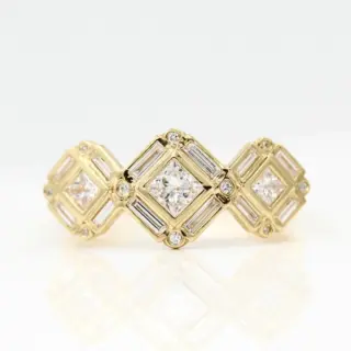 The Darby engagement ring on finger — modern three-stone design with halo, in yellow gold