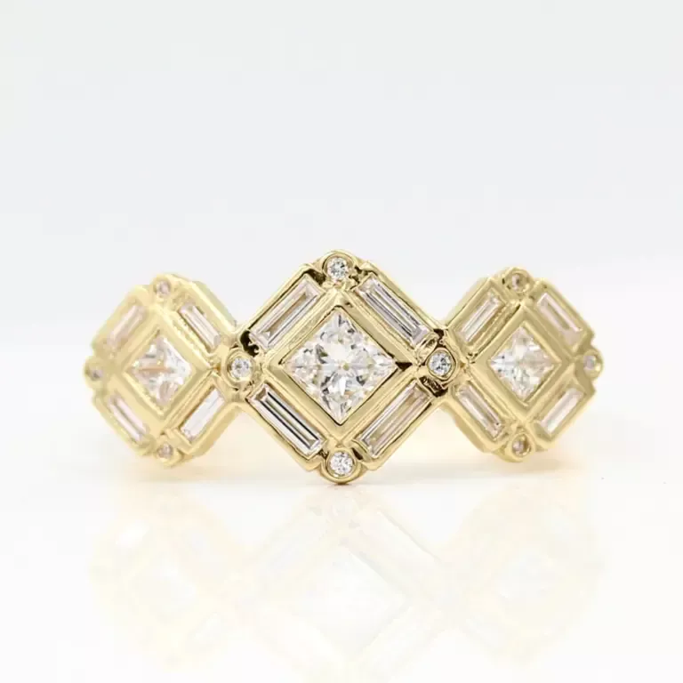 The Darby engagement ring on finger — modern three-stone design with halo, in yellow gold