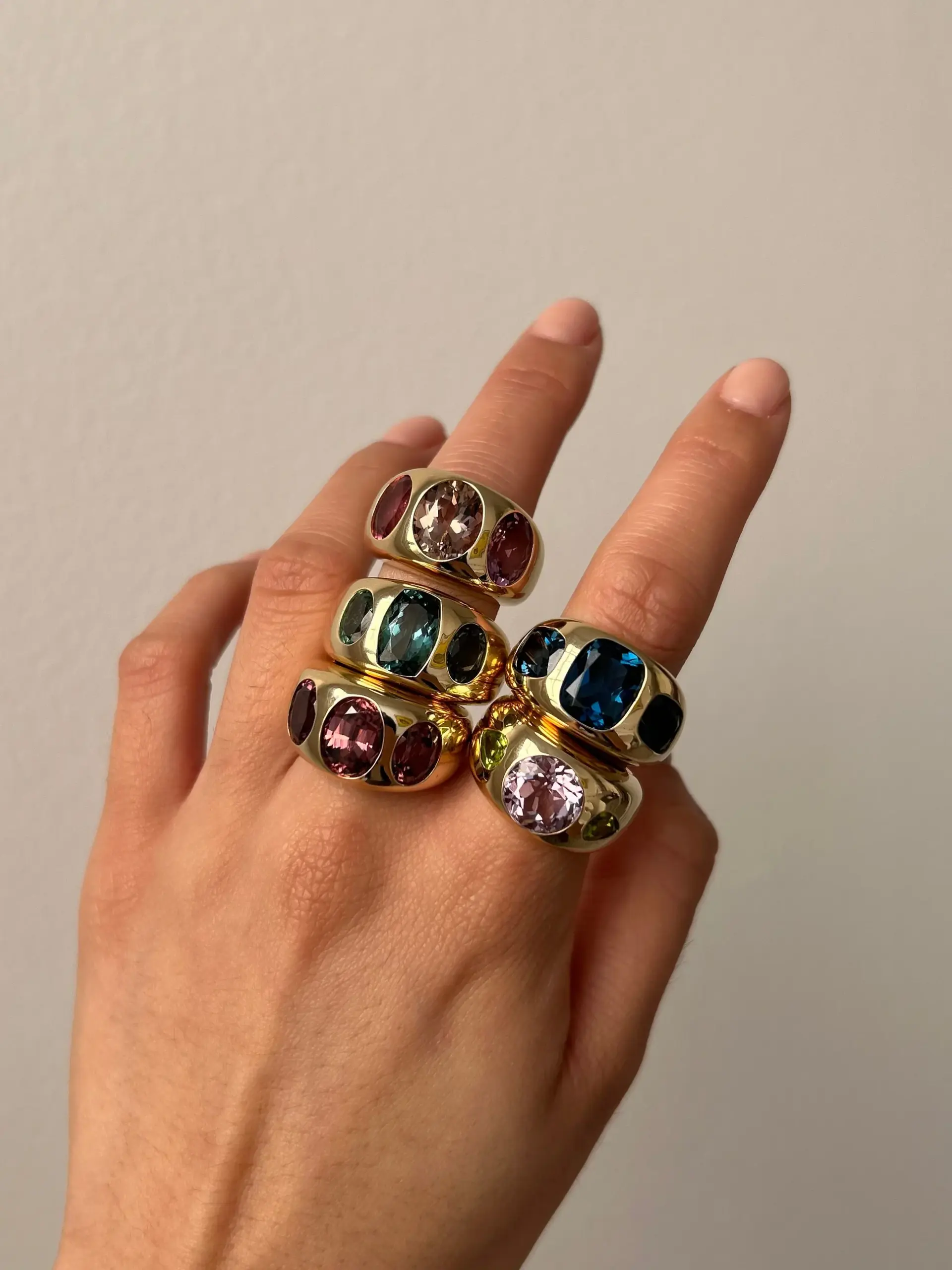 The chunky Nomad ring on a finger, highlighting the vibrant green peridot and icy aquamarine set in polished yellow gold.