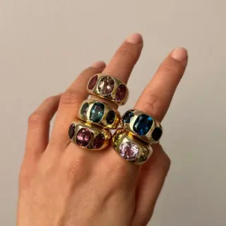 The chunky Nomad ring on a finger, highlighting the vibrant green peridot and icy aquamarine set in polished yellow gold.