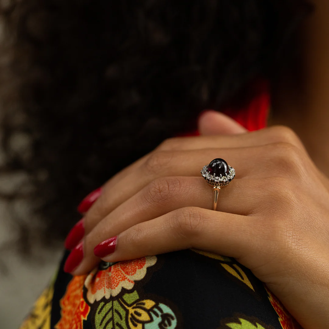Close‑up of Victorian circa 1870s–1890s garnet cabochon ring surrounded by 12 Old‑Mine‑cut diamonds in silver‑topped 10k gold setting