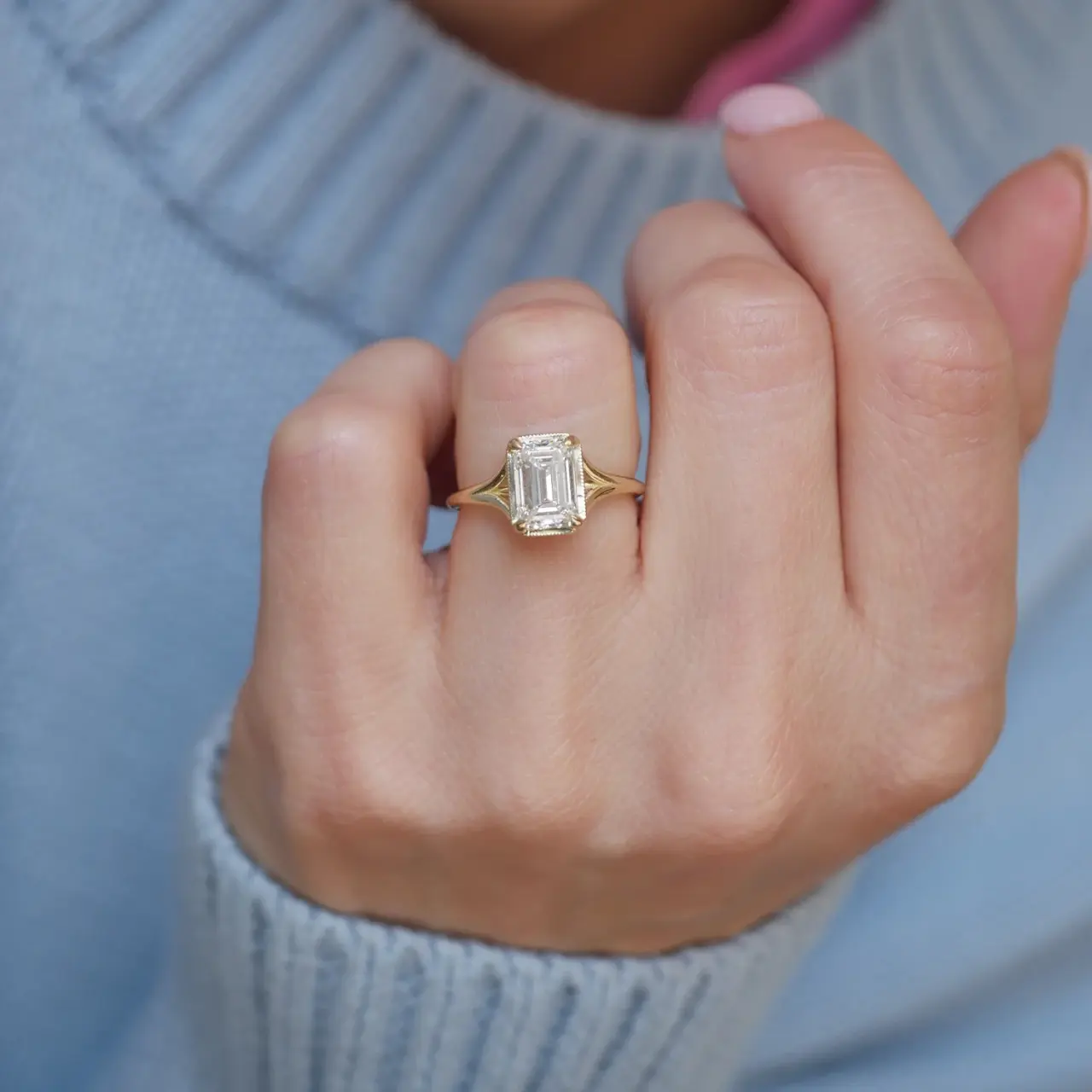 Model’s hand wearing Berlinger Jewelry’s split‑shank emerald‑cut diamond solitaire in 14K yellow gold, highlighting the elegant band split and radiant center stone