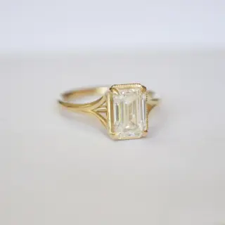 Side profile of split‑shank emerald‑cut diamond solitaire ring, showing the bridged band that separates beneath the center stone and accent details in 14K yellow gold