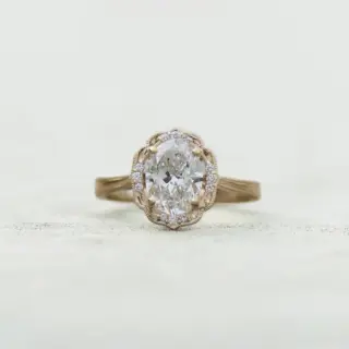 14k yellow gold Daisy Blossom engagement ring with 1.16 carat oval lab-grown diamond and halo of twelve accent diamonds with milgrain detail.