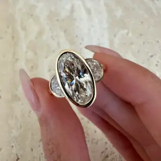 Orianne three‑stone ring on finger, with oval lab‑grown diamond and half‑moon accents in a warm yellow gold bezel.