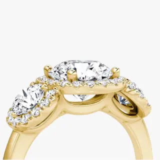 Close-up of VRAI three‑stone halo ring showing round center diamond with two trapezoid side stones and halo detail.