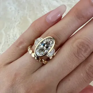 Close-up of Orianne three‑stone ring showing bezel-set oval center diamond flanked by half‑moon diamonds in gold.