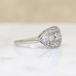 Close-up of Art Deco ‘Eye’ ring showcasing three graduated old-cut diamonds framed by a halo of smaller stones in a curved white gold setting