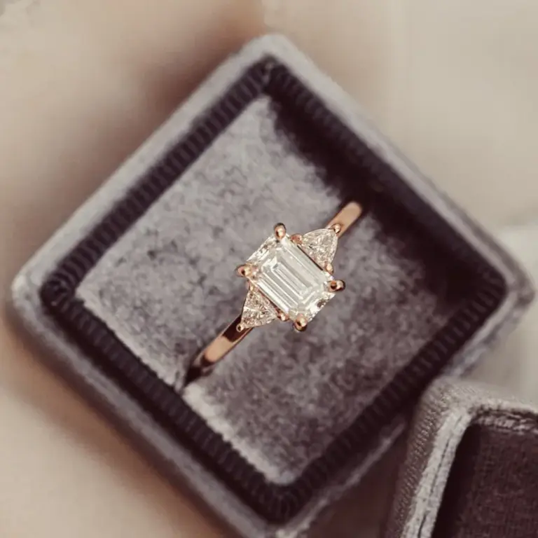 Barbara Maison three-stone engagement ring in gold featuring a 1.0 ct emerald‑cut moissanite center flanked by 0.26 ct trillion‑cut moissanites