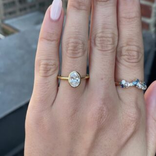 Elegant engagement ring featuring an oval diamond encircled by a contoured bezel for a modern minimalist look.