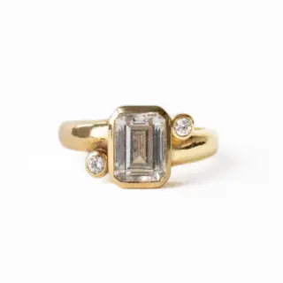 Front view of the Indigo Emerald Ring by June Rings, showcasing a 1.55ct emerald-cut center stone with .06ctw side stones, set in a 3.7mm domed band.